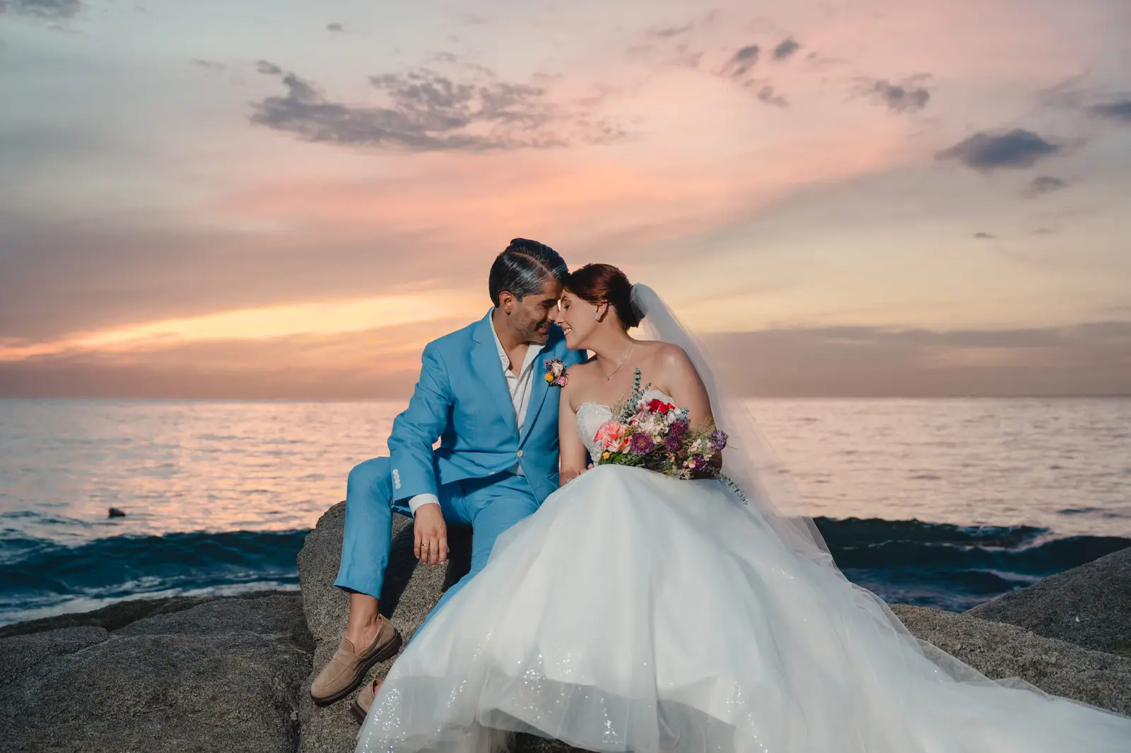 Novios sentados sobre las rocas frente al mar al atardecer en Santa Marta